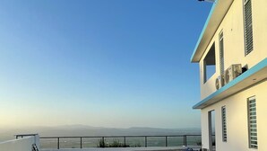 A rooftop terrace with a clear view of distant mountains, a metal railing, and a few scattered items.