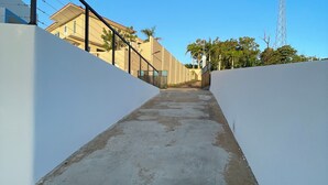 A concrete pathway flanked by white walls, leading towards a building with a red-tiled roof.