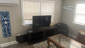 Una sala de estar con televisor de pantalla plana sobre un mueble, un tapete estampado y una mesa de centro de madera.