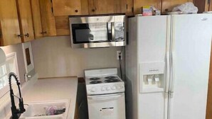 Una cocina compacta con armarios de madera, un microondas, una estufa y un refrigerador.