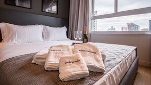 Une chambre d’hôtel avec un lit, deux serviettes ornées de l’inscription « Brazilian Corner », une bouteille de champagne et deux verres.