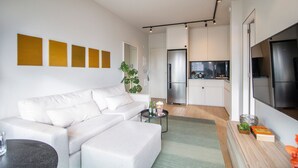 Un salon moderne avec un canapé blanc, une petite table basse et une cuisine en arrière-plan.