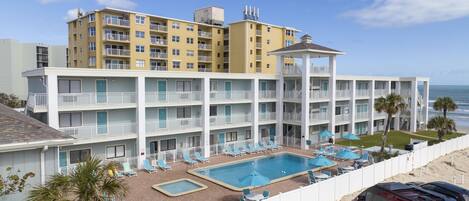 A multi-story hotel with a pool area, including lounge chairs and umbrellas.