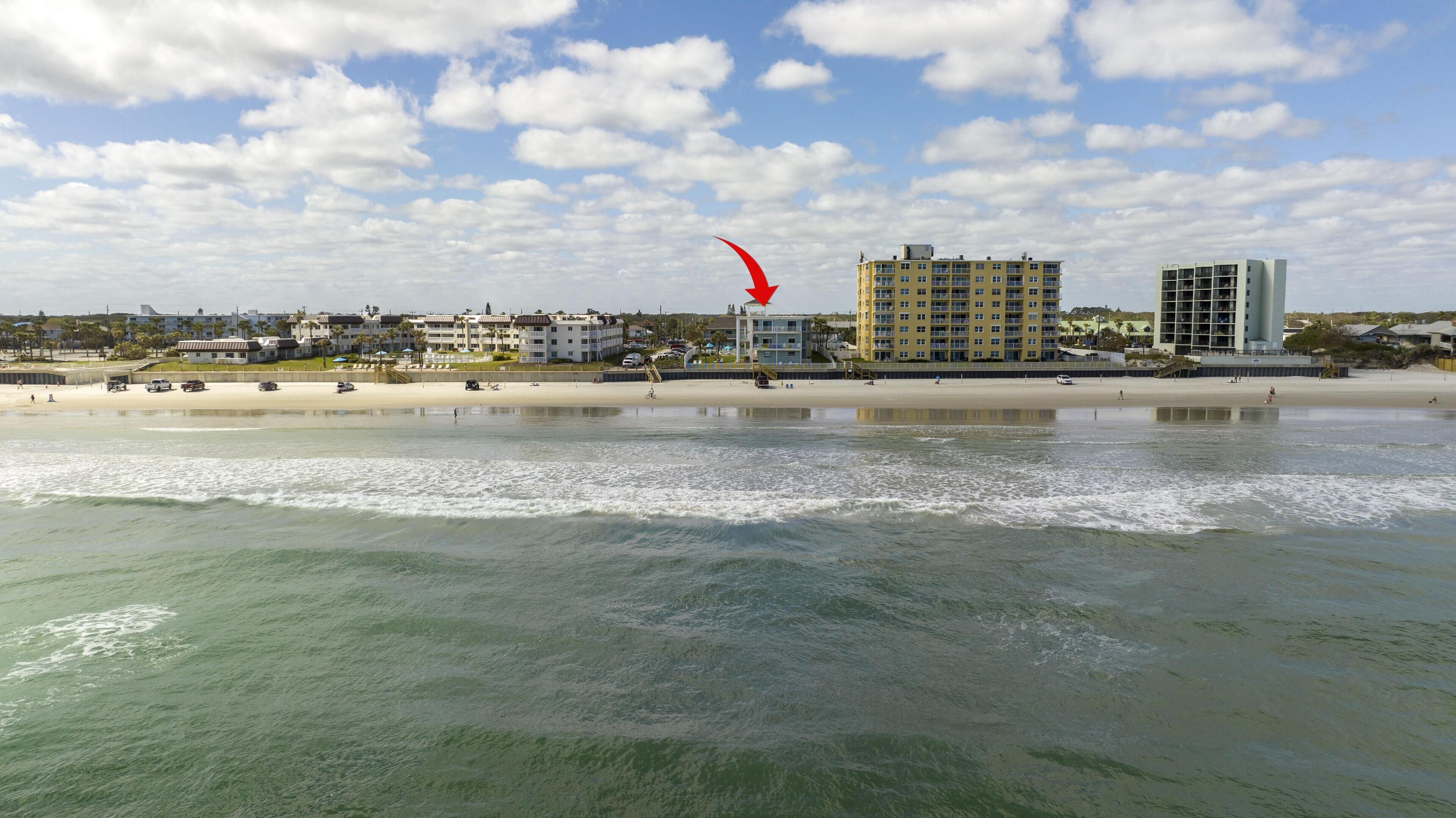 A coastal hotel with multiple floors, a beach in the foreground, and a clear sky.