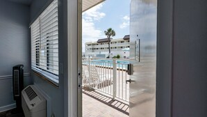 A room with a view of a pool, a balcony, and a building with multiple balconies in the background.