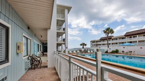 A hotel balcony with a pool, white railings, and a view of the pool area.