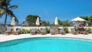 Une piscine entourée d’une clôture et de palmiers, avec des chaises longues et des parasols.