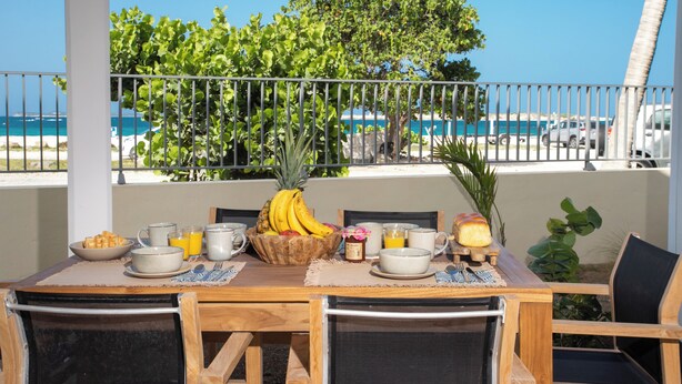 Une table de petit-déjeuner avec des fruits, des boissons et une vue sur l’océan et la plage.