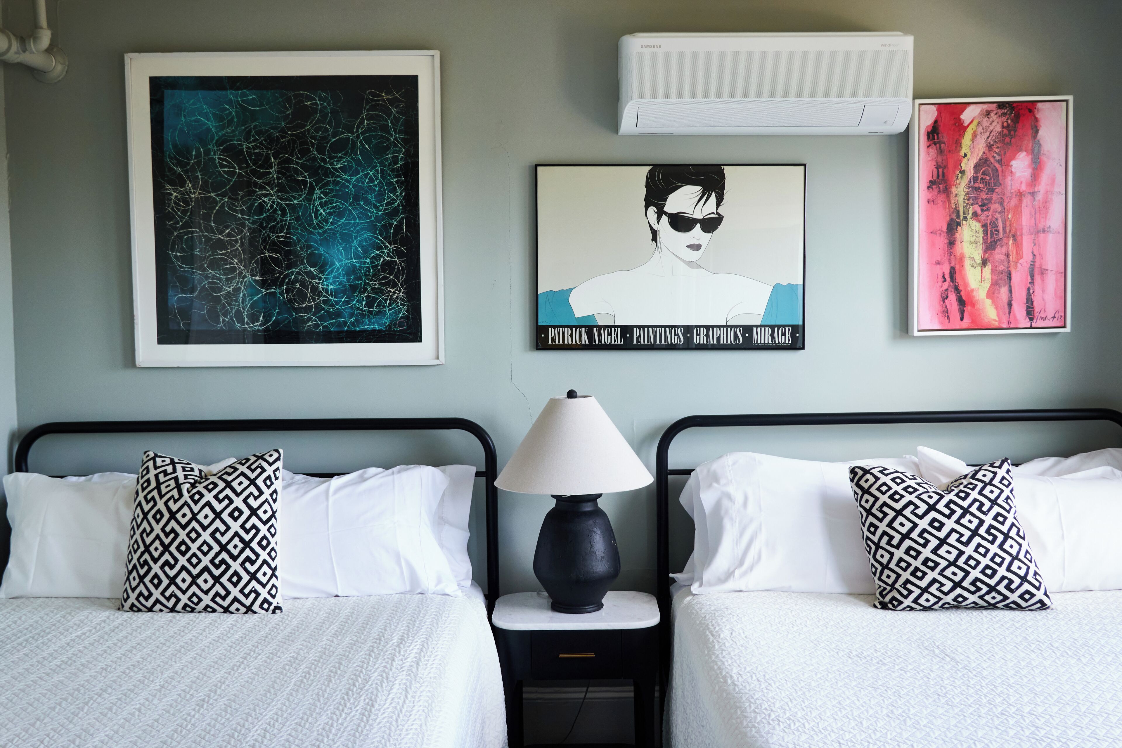 Une chambre d’hôtel avec deux lits, une table de chevet avec une lampe et des œuvres d’art accrochées aux murs.