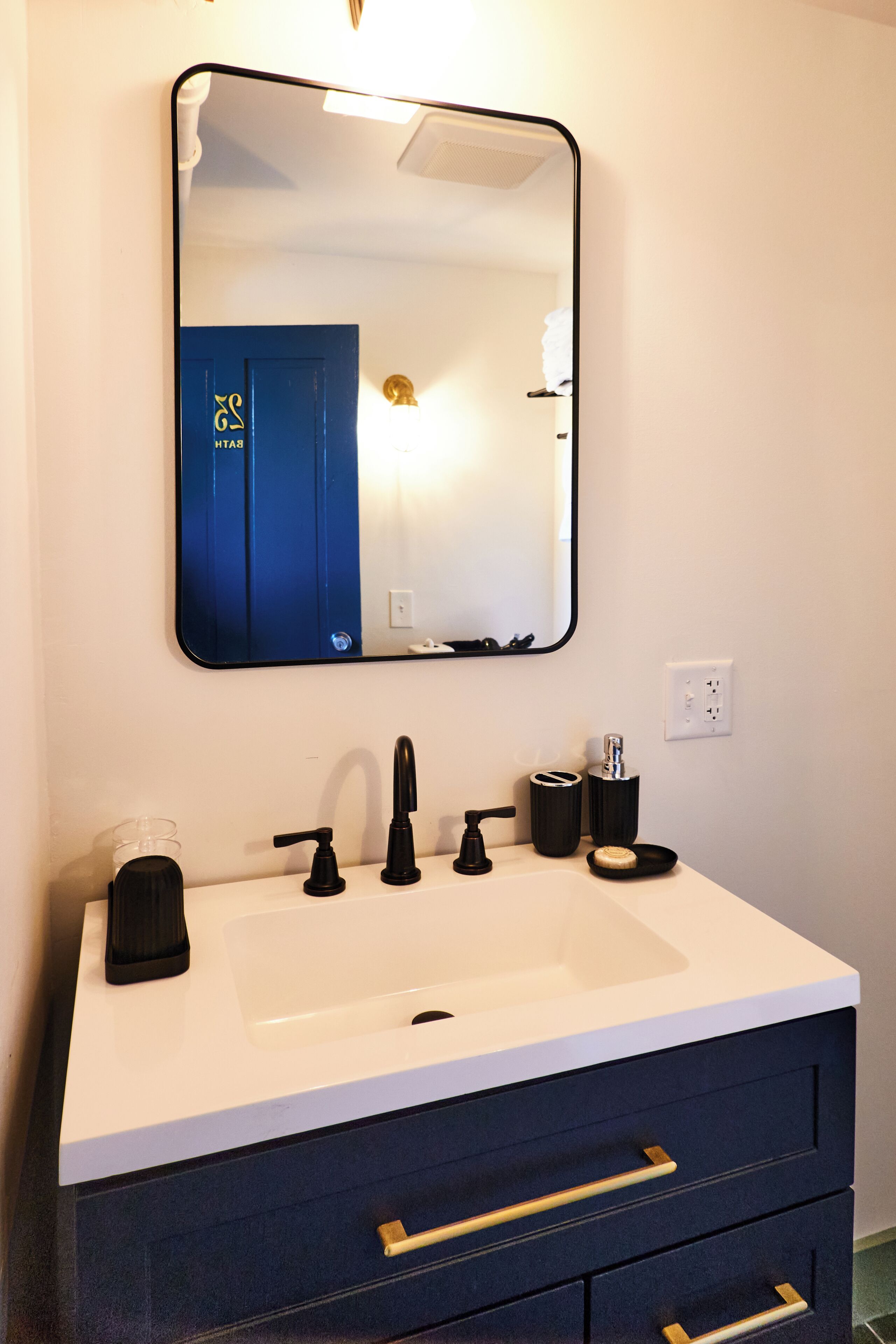 Un baño con lavamanos blanco, grifo negro y mueble azul con cajones.