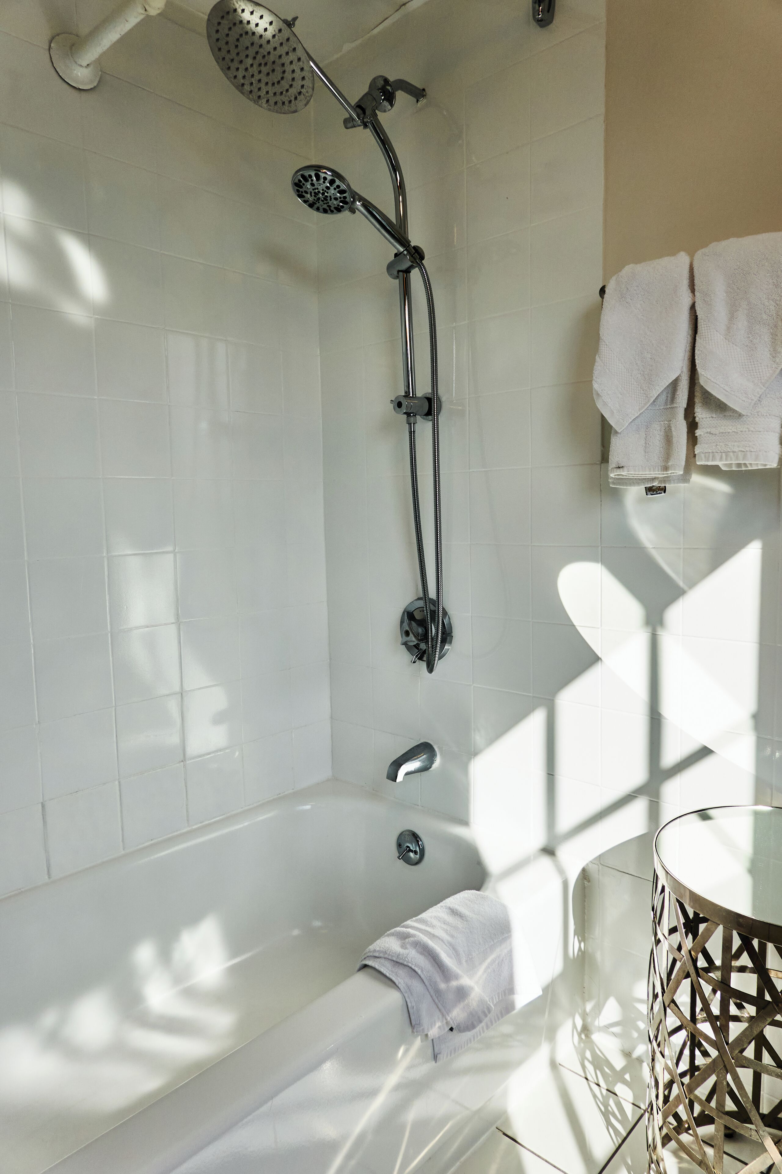 A modern bathroom with a bathtub, a shower with a handheld showerhead, and a glass-enclosed sink.