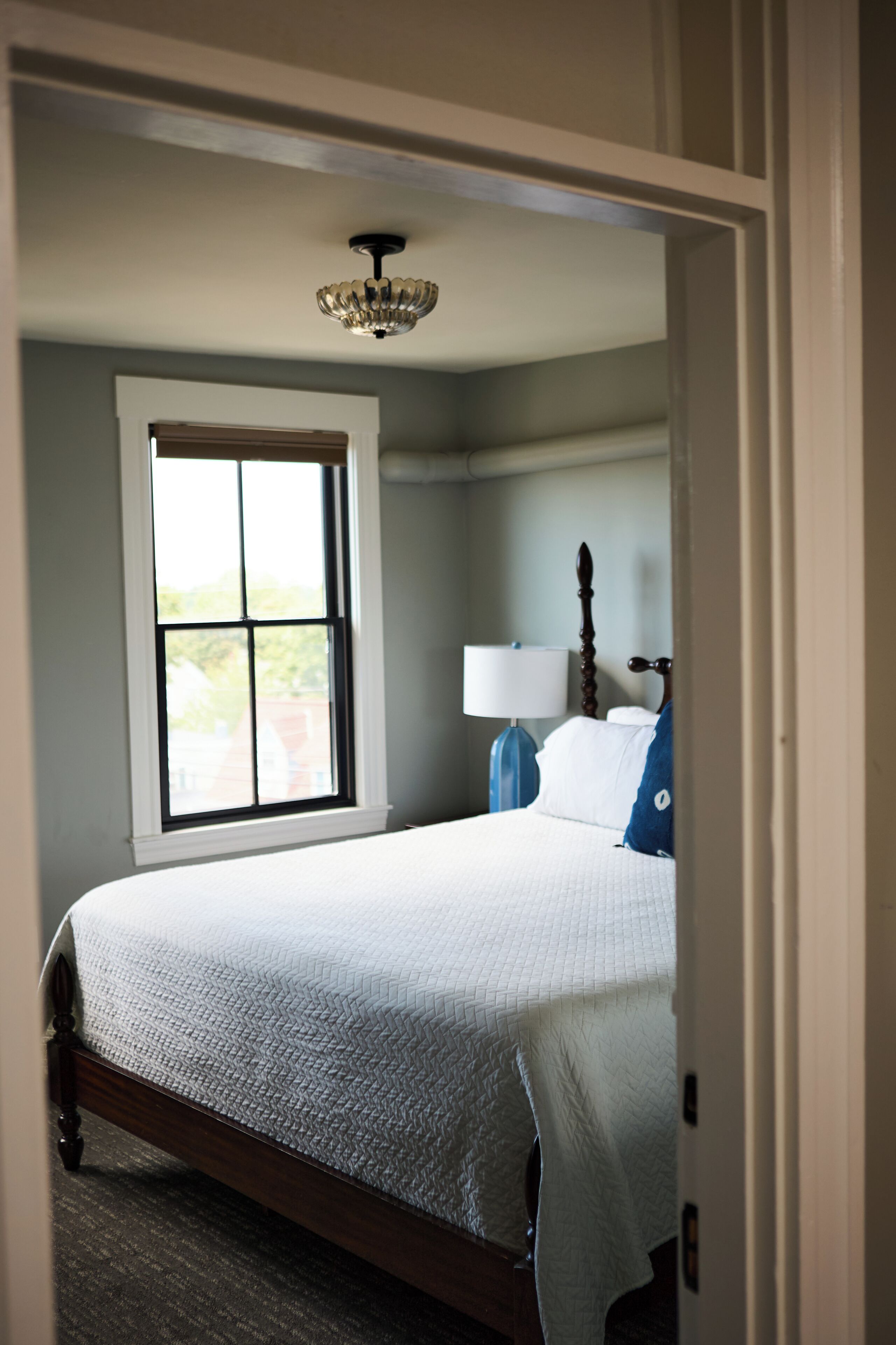 A bedroom with a bed, a window, a lamp, and a ceiling light fixture.