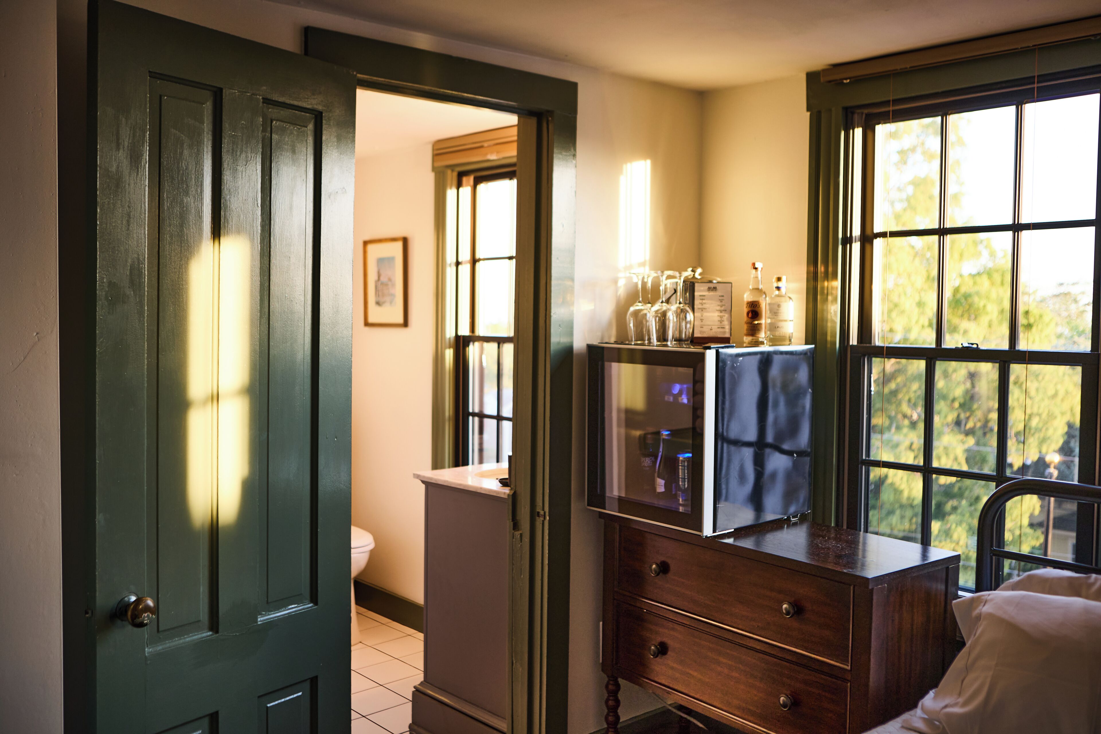 A room with a wooden dresser, a window with a view, and a door leading to another room.