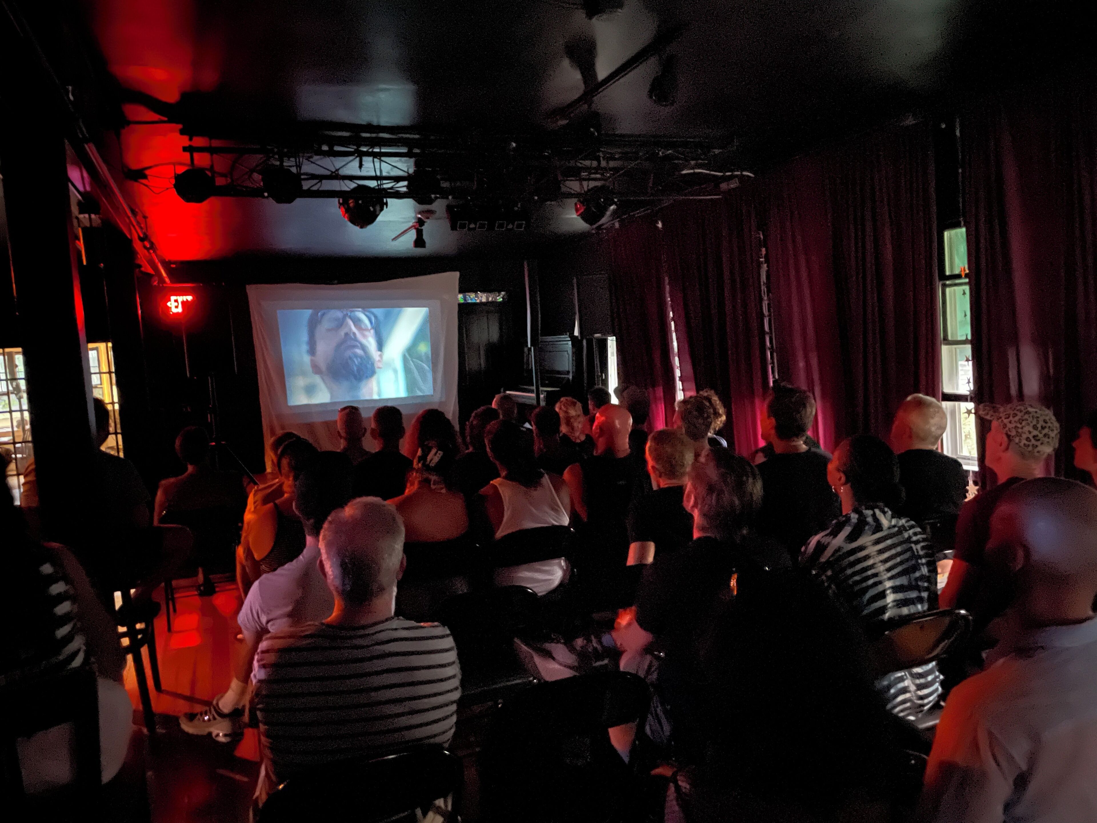 Un grupo de personas sentadas en una habitación con poca luz, mirando una pantalla grande que muestra una escena de cine.