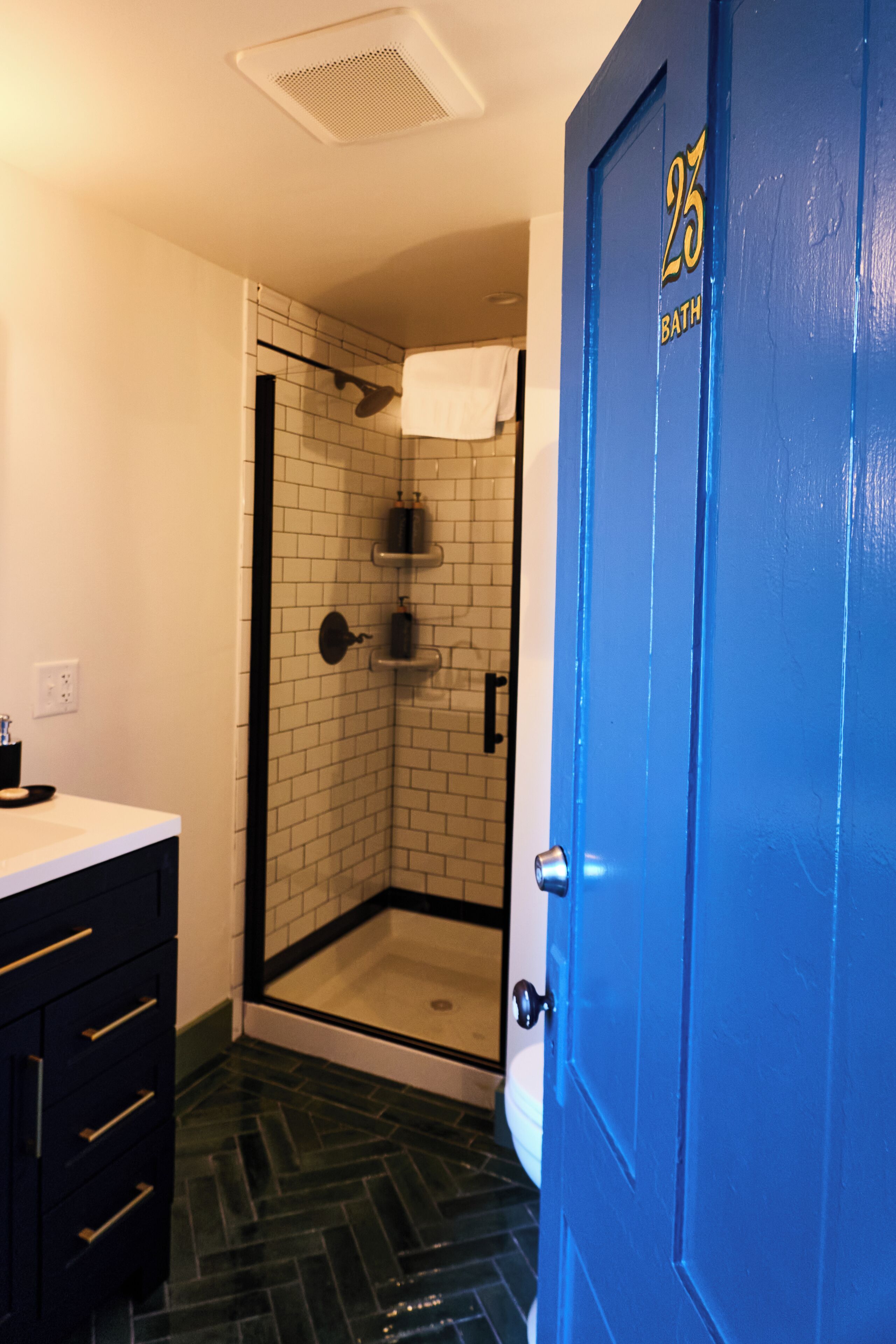 Une salle de bain avec une douche, un lavabo et une porte bleue portant un numéro.