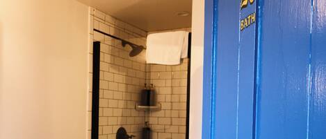 A bathroom with a shower, a sink, and a blue door with a number.