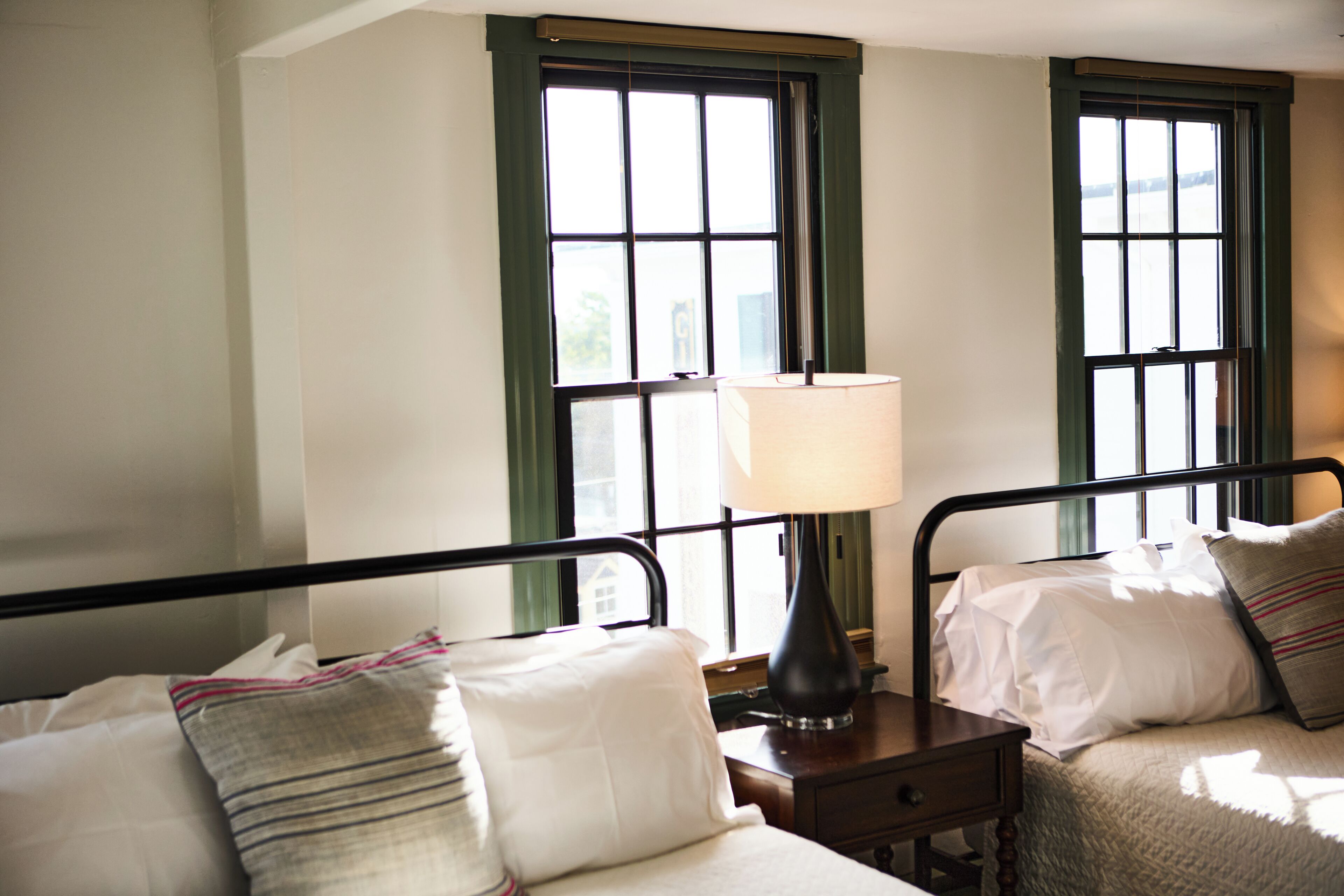 A room with two beds, each with a pillow and a bedside table with a lamp.