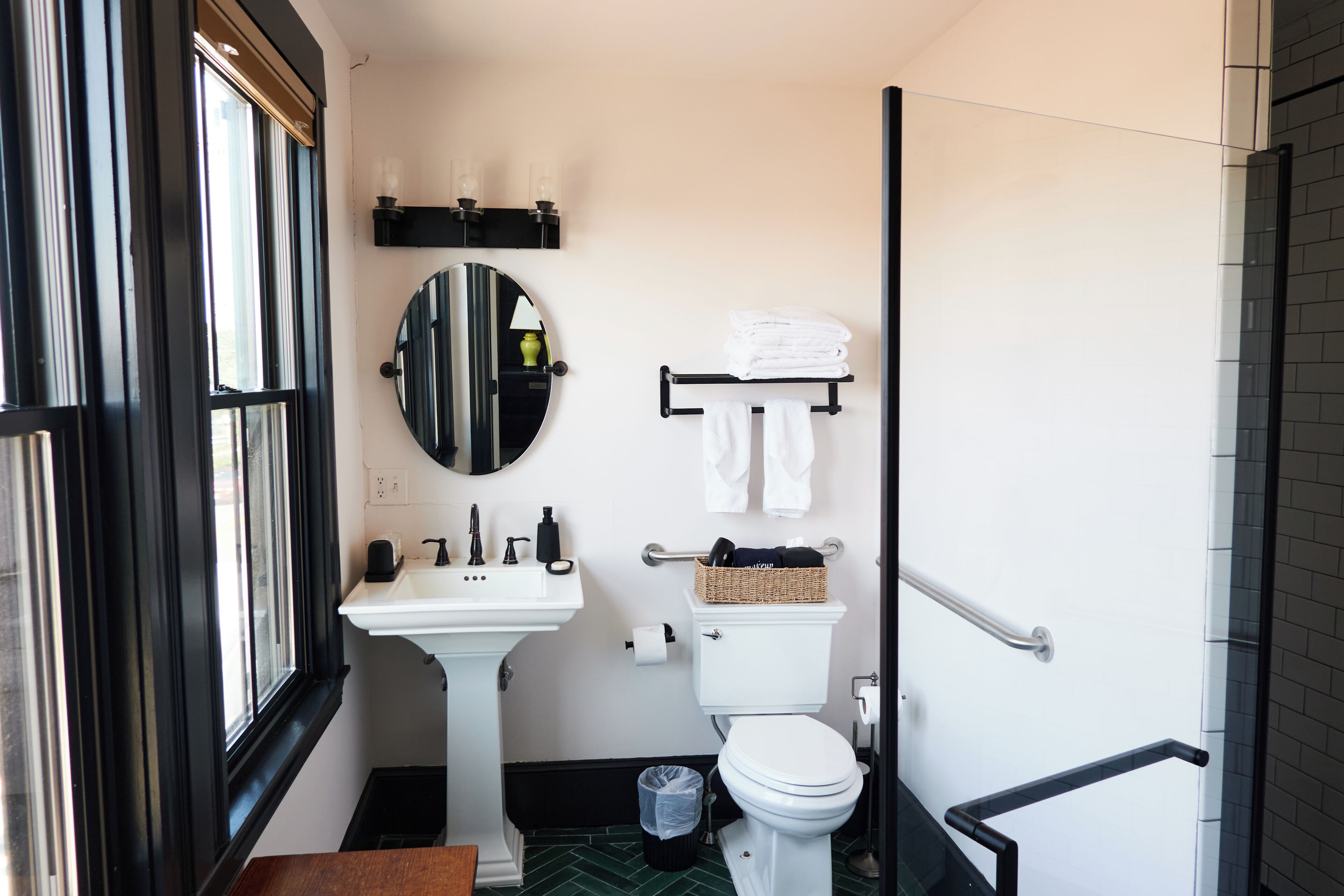 A modern bathroom with a white sink, round mirror, toilet, and a towel rack.