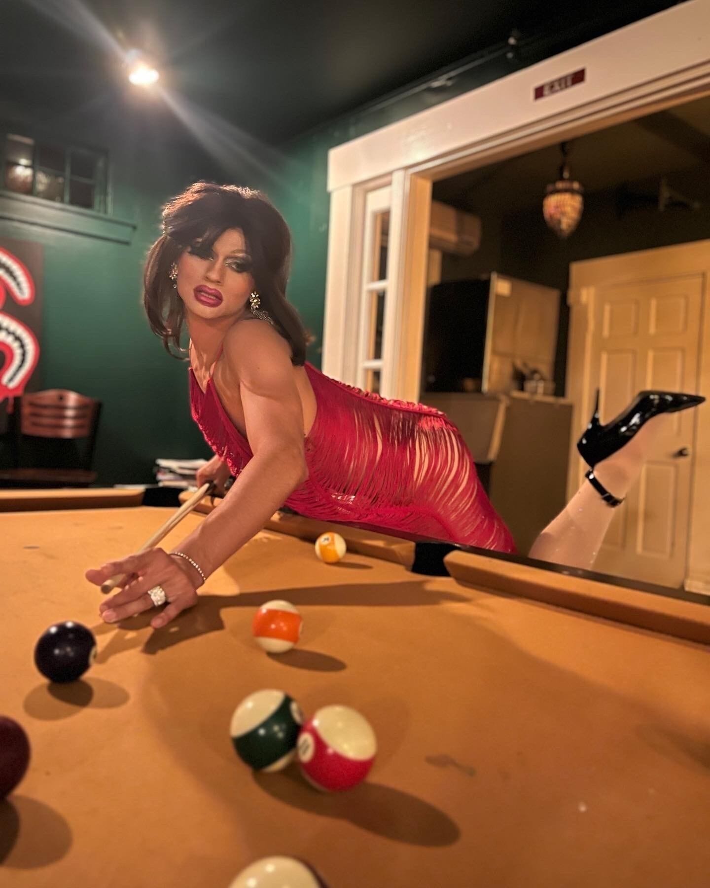 A person playing pool in a room with a green wall, a pool table, and a door in the background.