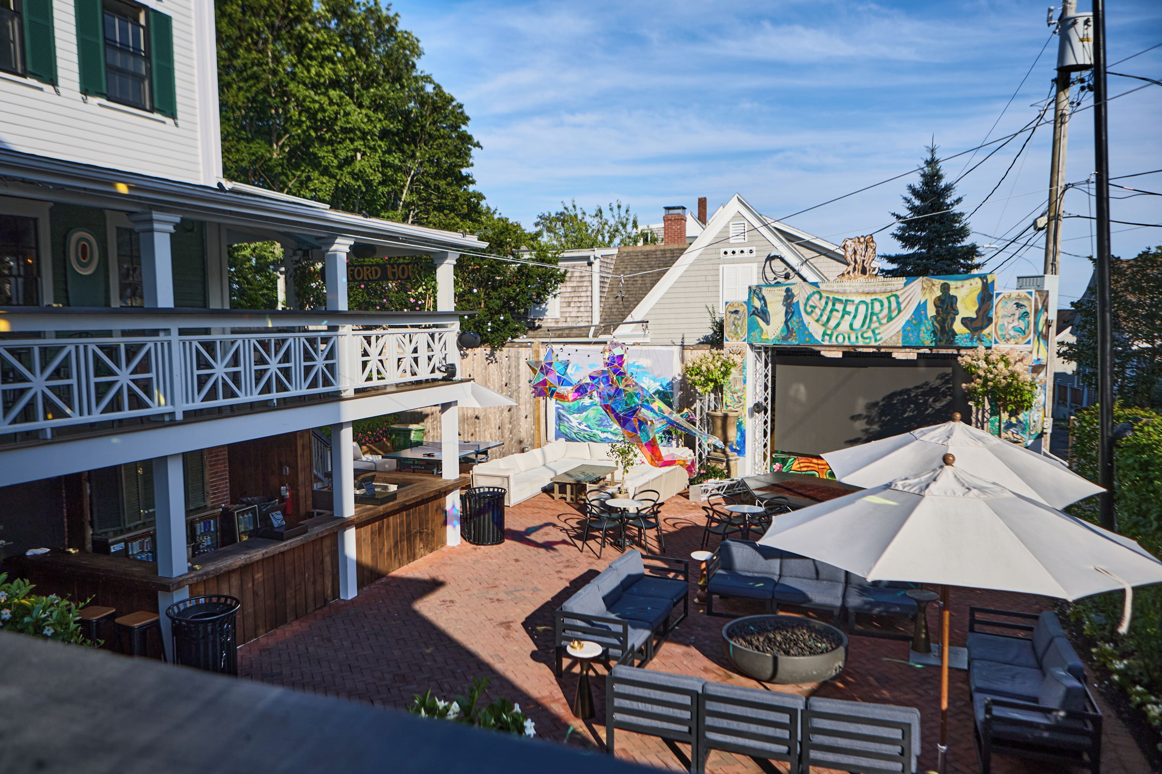 Un espace extérieur aménagé avec des tables et des chaises, un foyer et une fresque murale sur le bâtiment.