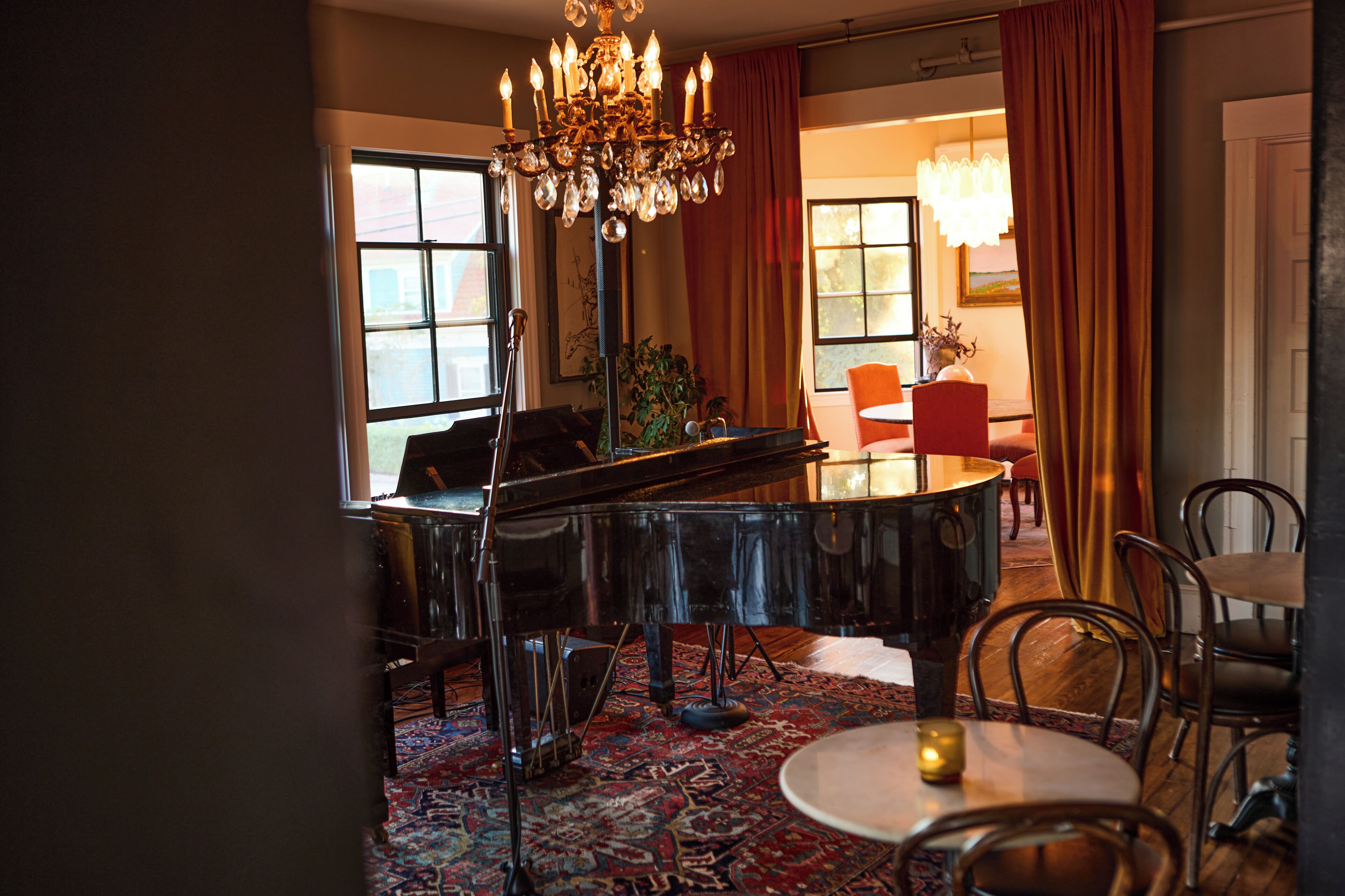 A room with a grand piano, a chandelier, and a dining area with chairs and a table.