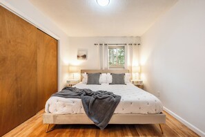 Una camera da letto con un letto grande, due comodini con lampade, una finestra con tende e un pavimento in legno.