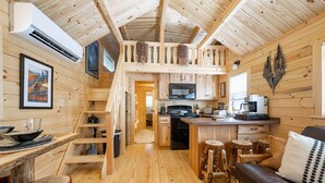 L’intérieur d’un chalet en bois comprend une cuisine, un coin repas et une chambre à coucher située en mezzanine.