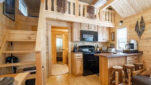 L’intérieur d’une cabane en bois comprend un coin cuisine, des tabourets en bois, un canapé et un escalier menant à une mezzanine.