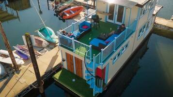 Een vlot huis met terras, buitenmeubilair en boten afgemeerd in de buurt.