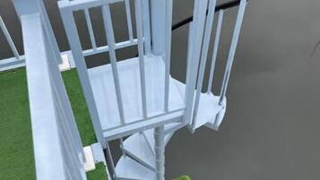 A white metal staircase with a handrail leading up to a platform with green artificial grass.