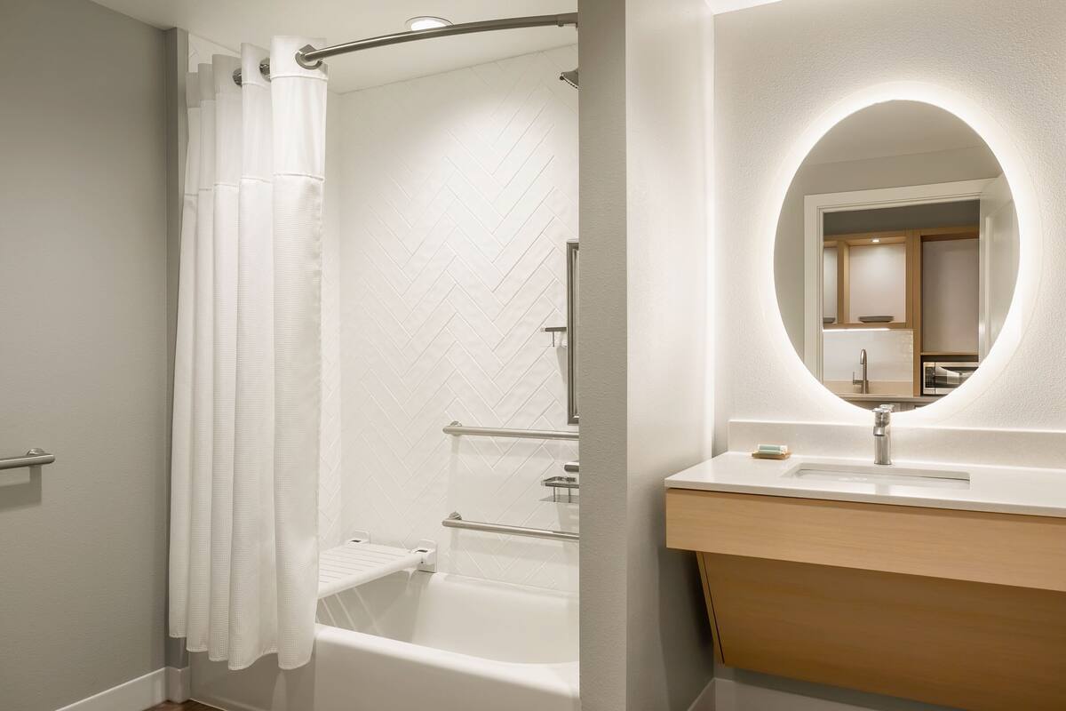 Een moderne badkamer met een badkuip, douchegordijn, wastafel met spiegel en een handdoekrek.