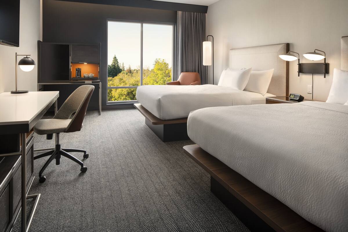 A hotel room with two beds, a desk, a chair, and a TV.