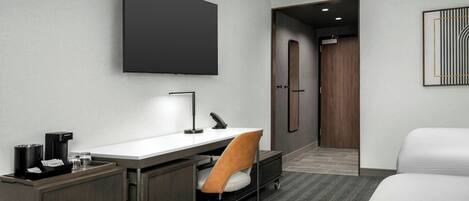 A hotel room with a desk, chair, bed, and a flat-screen TV.
