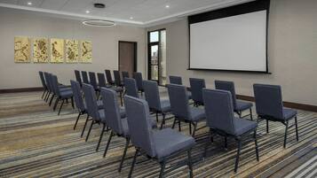 A conference room with rows of chairs, a projector screen, and abstract art on the wall.