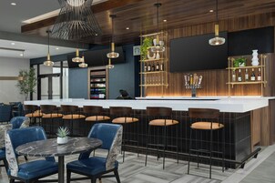 Zona de bar moderna con una mesa de mármol, sillas azules y una variedad de botellas en estantes.