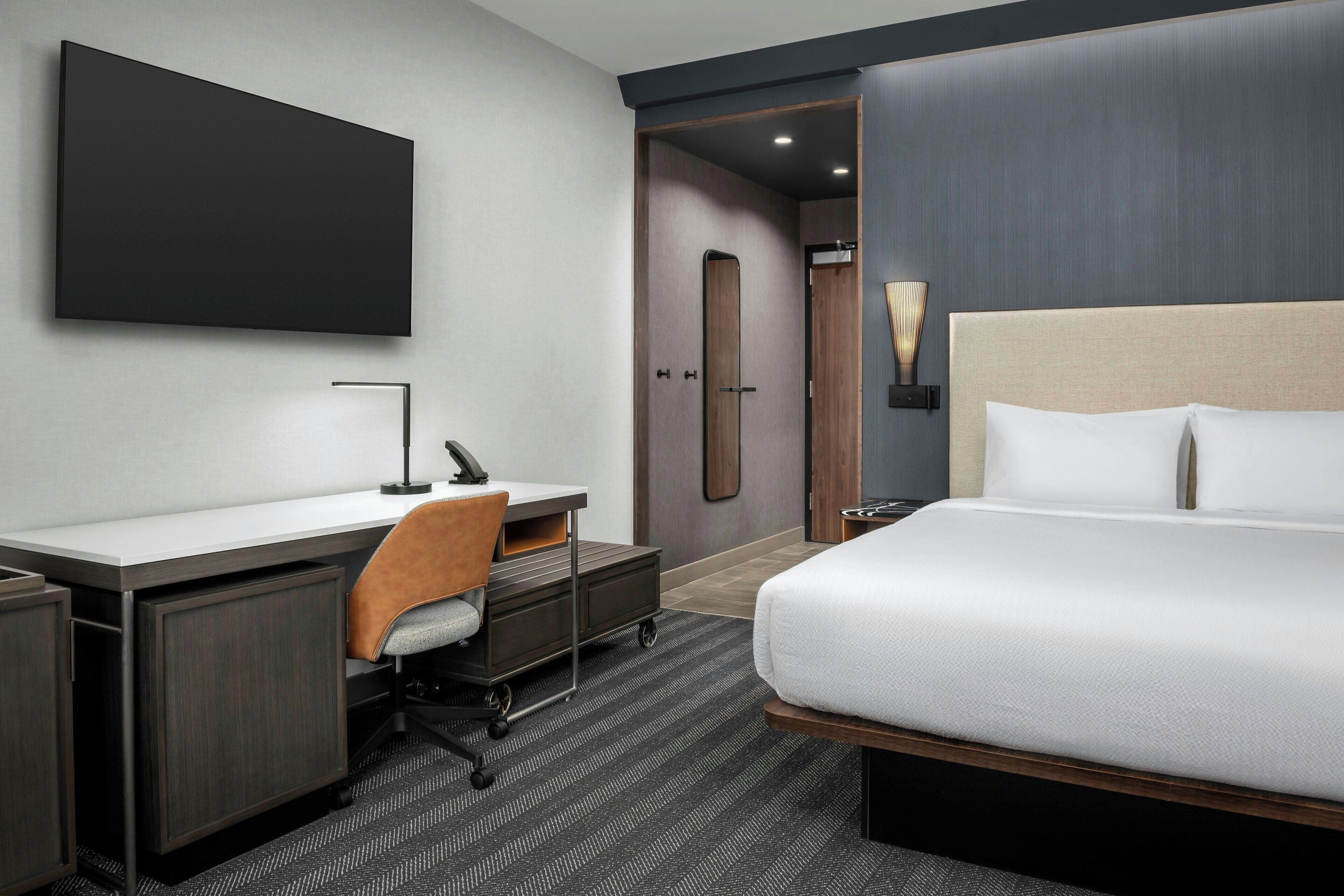 Quarto de hotel moderno com uma cama grande, uma escrivaninha com cadeira, televisão de tela plana e um closet espaçoso.