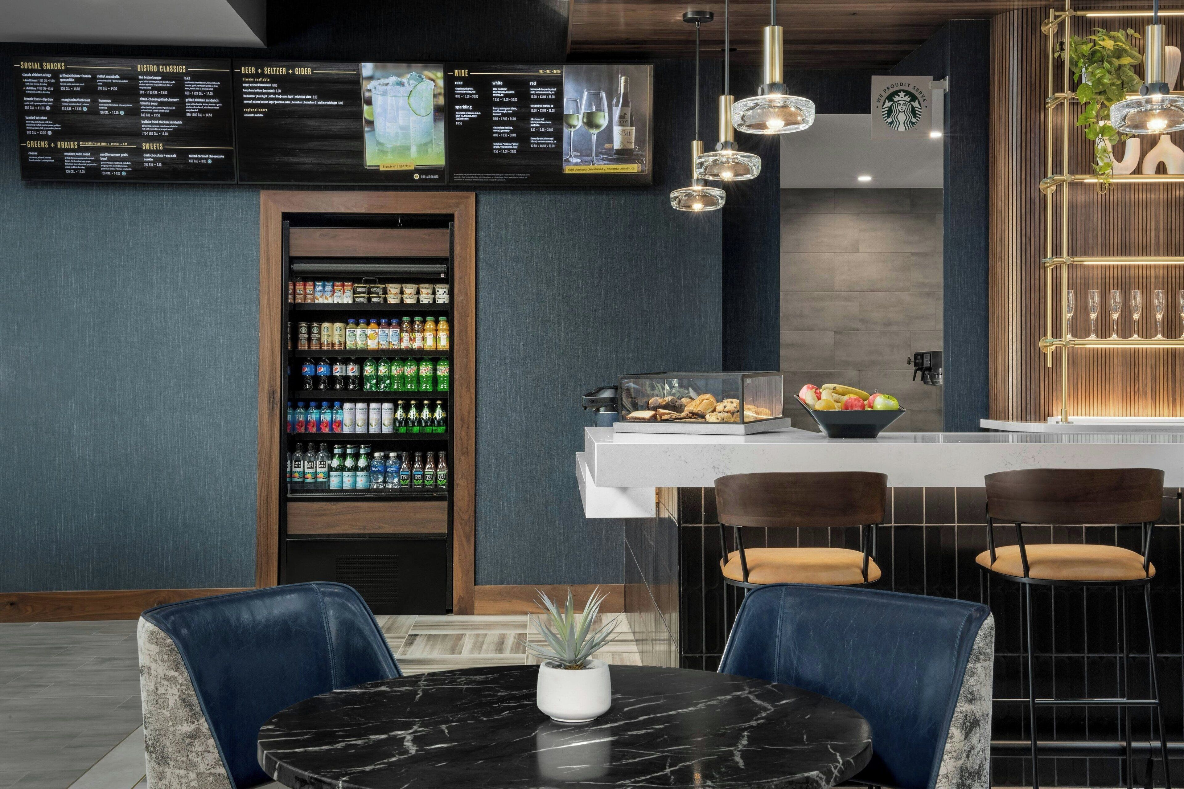 A modern bar area with a menu board, beverage dispensers, and seating.