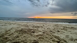 Une plage avec un coucher de soleil en arrière-plan et un ciel nuageux.