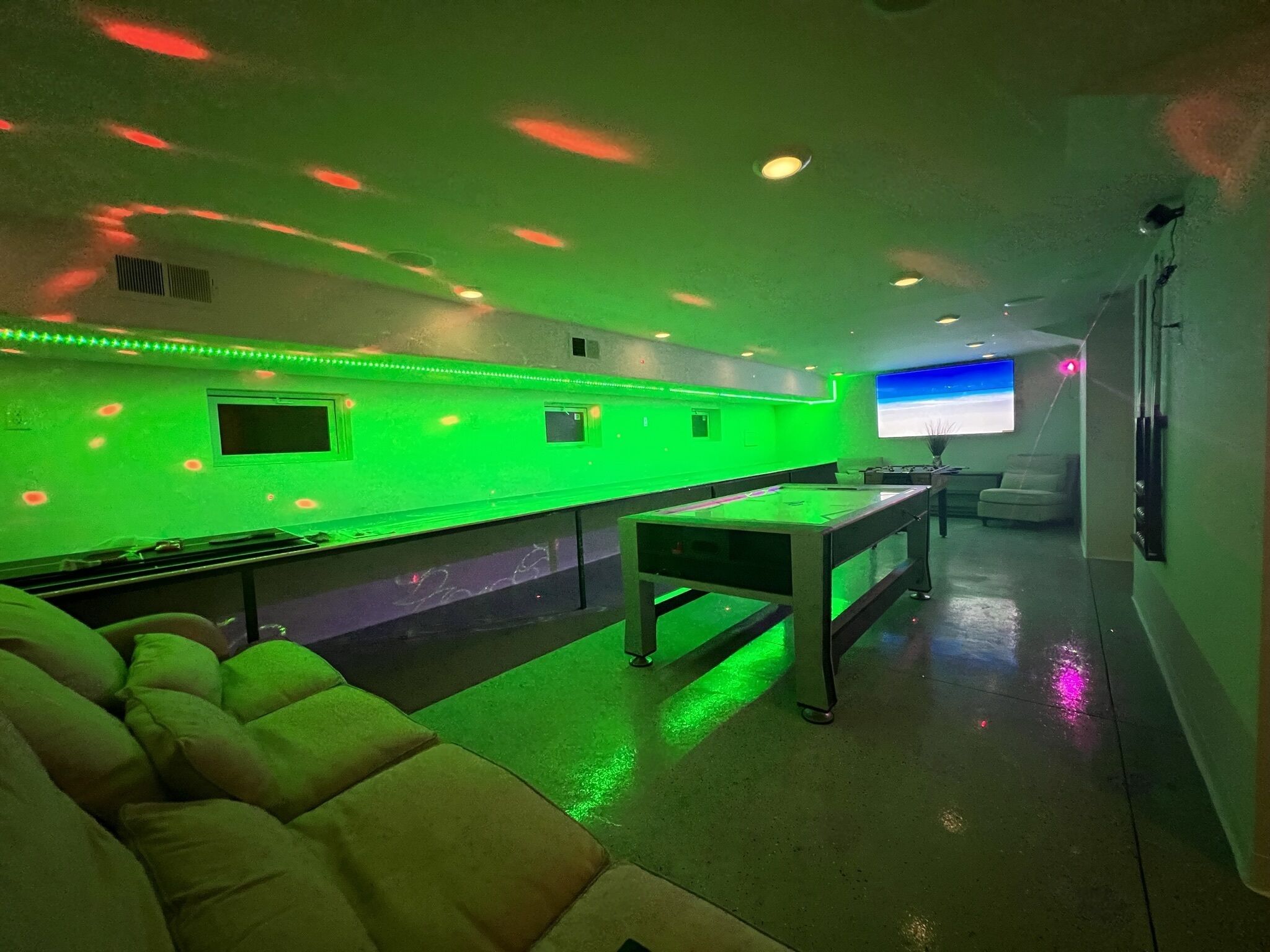 A room with a green-lit bar area, a flat-screen TV, and a sofa.