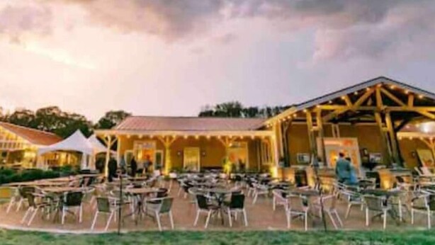 Un espace extérieur aménagé pour les repas, avec des tables et des chaises, un coin salon abrité et un bâtiment à la façade jaune.