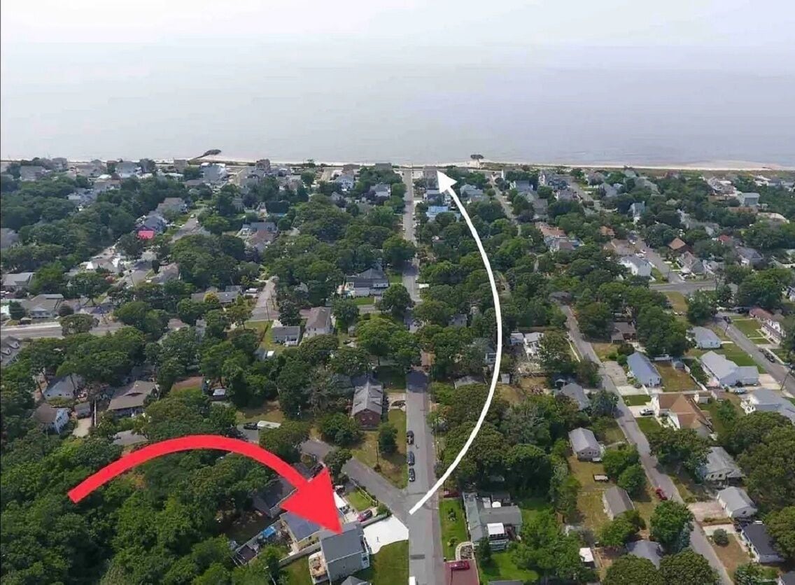Luchtbeeld van een woongebied met huizen, wegen en een strand op de achtergrond.
