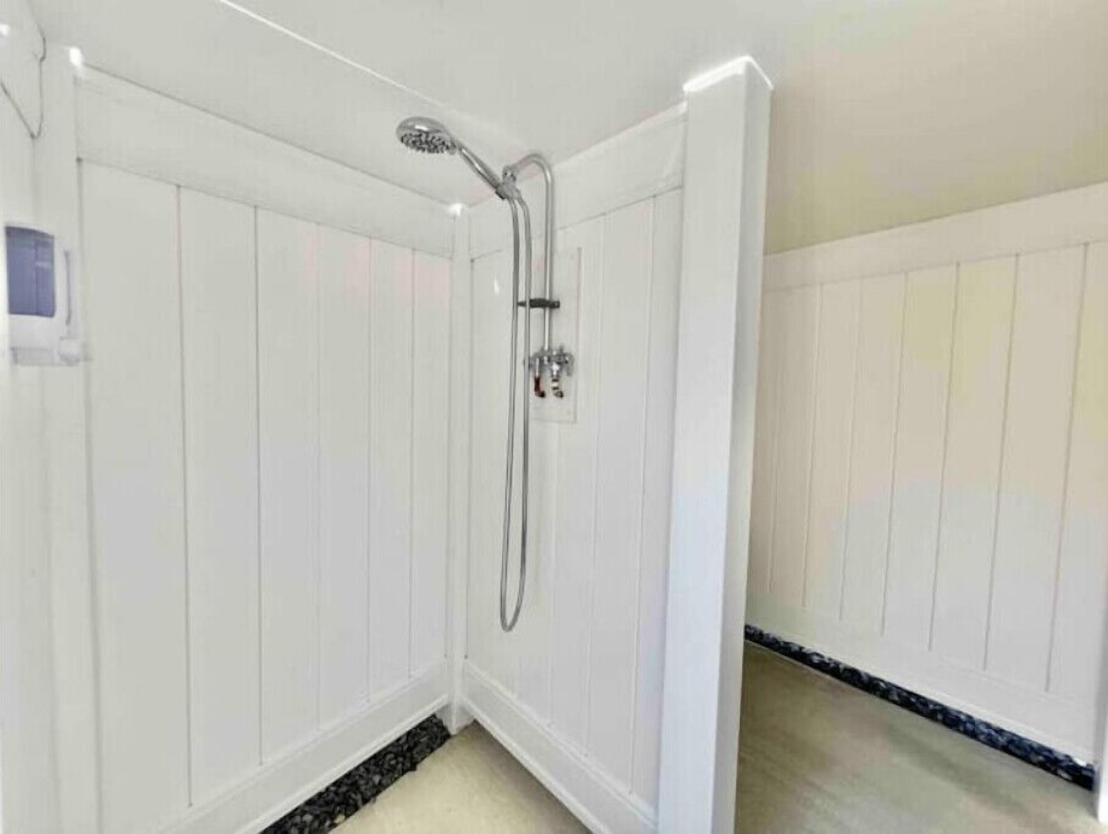 Un bagno con pareti bianche a pannelli, una doccia con soffione manuale e un piccolo pannello di controllo a parete.