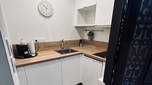 Una cocina pequeña con armarios blancos, encimera de madera, un lavabo, un reloj y una alfombra estampada.