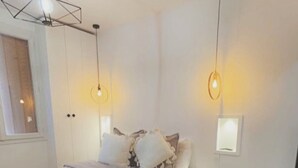 Un dormitorio con cama, almohadas, una manta y una disposición de toallas. Hay dos lámparas colgantes y una luz empotrada en la pared.