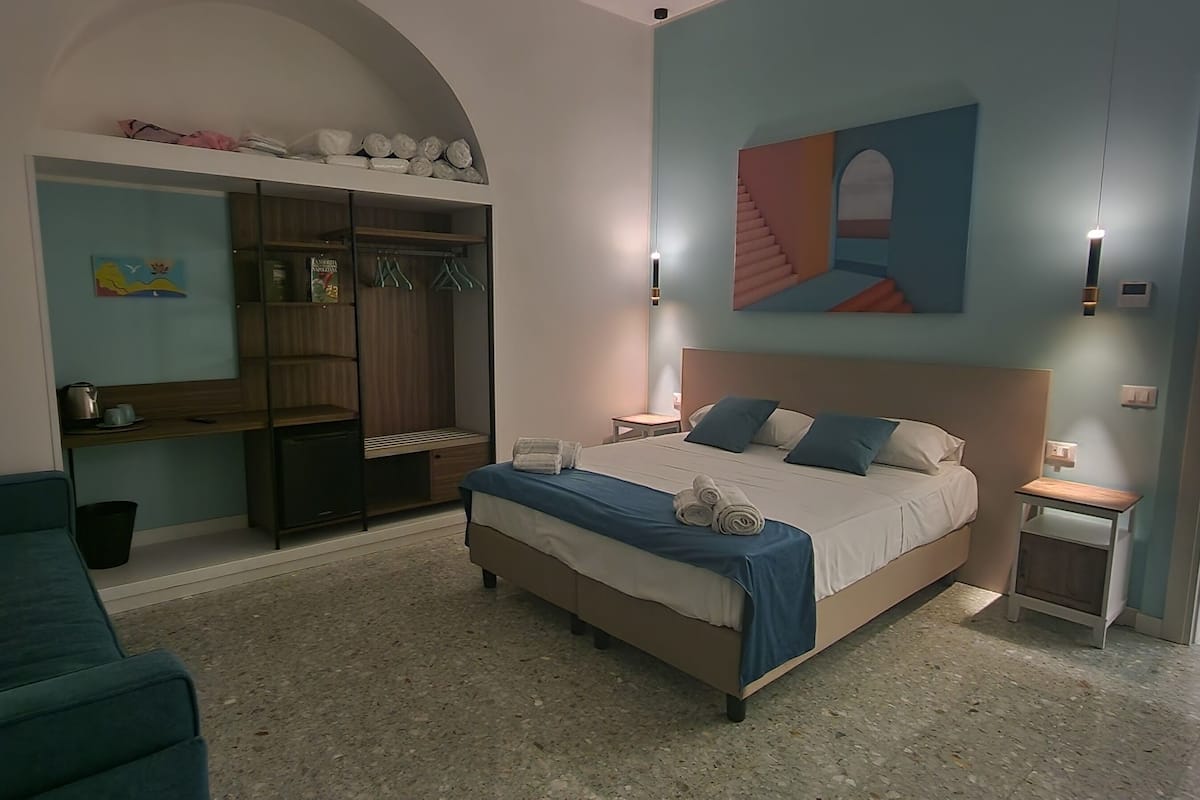 A bedroom with a bed, a sofa, a wardrobe, and a painting on the wall.