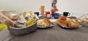 A table with various baked goods and packaged snacks, accompanied by several cups and a small plant on a shelf. - B&B la Dimora di Parthenope (Naples)