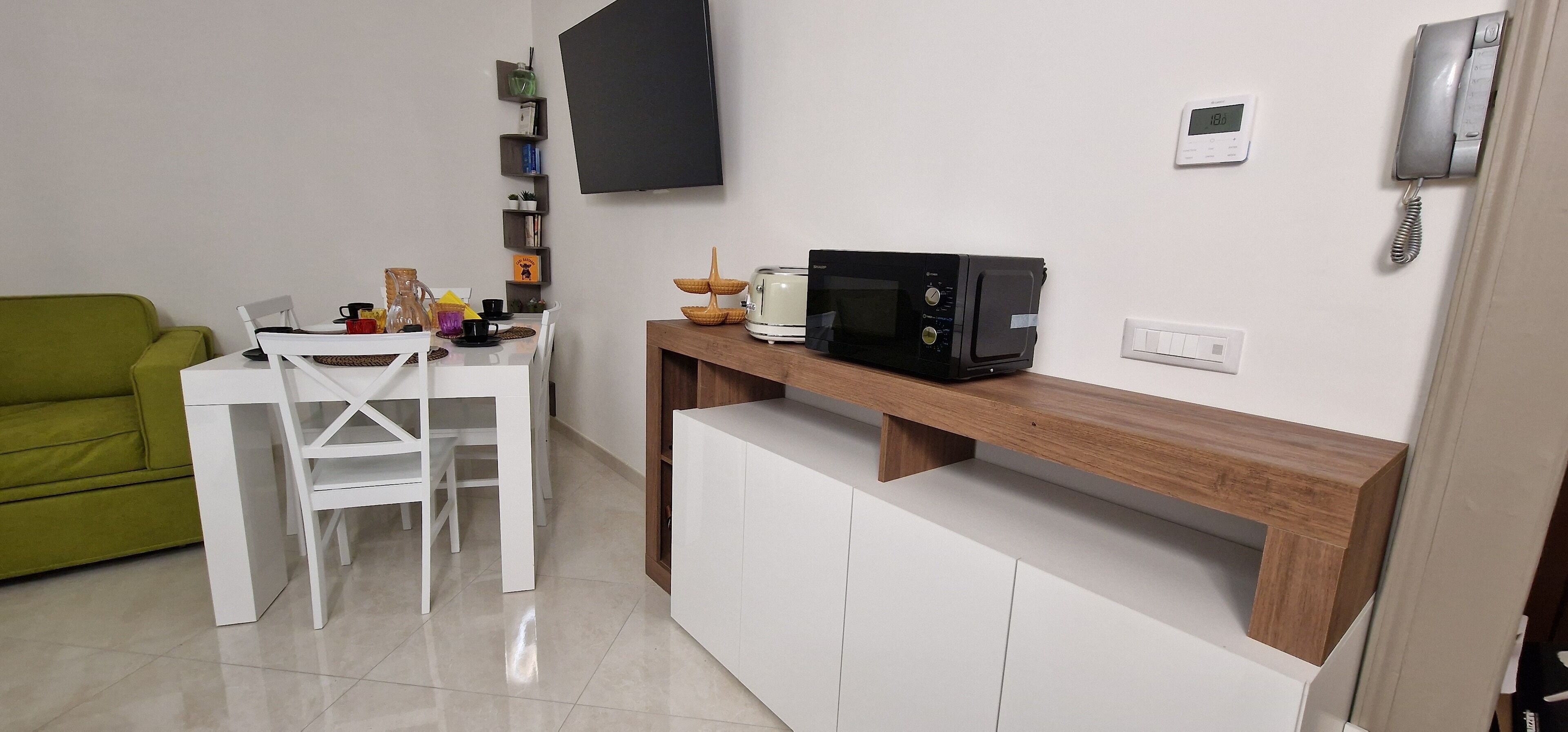 A compact living space with a dining area, a green couch, a white table, and a microwave on a wooden shelf.