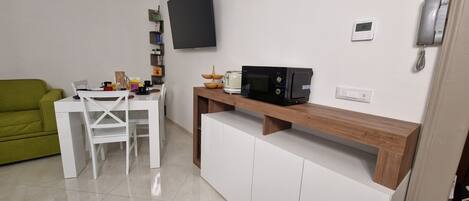 A compact living space with a dining area, a green couch, a white table, and a microwave on a wooden shelf.