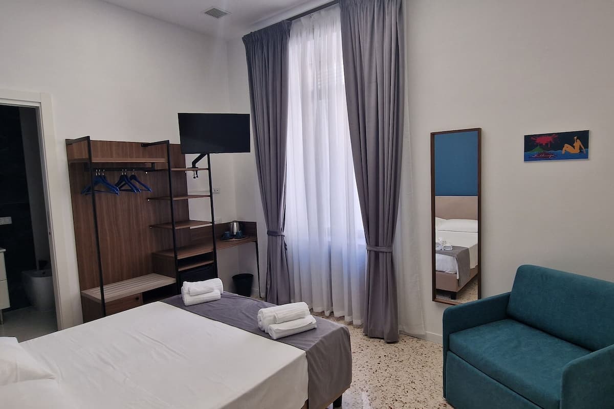 A hotel room with a bed, a desk, a chair, a wardrobe, a TV, and a window with curtains.