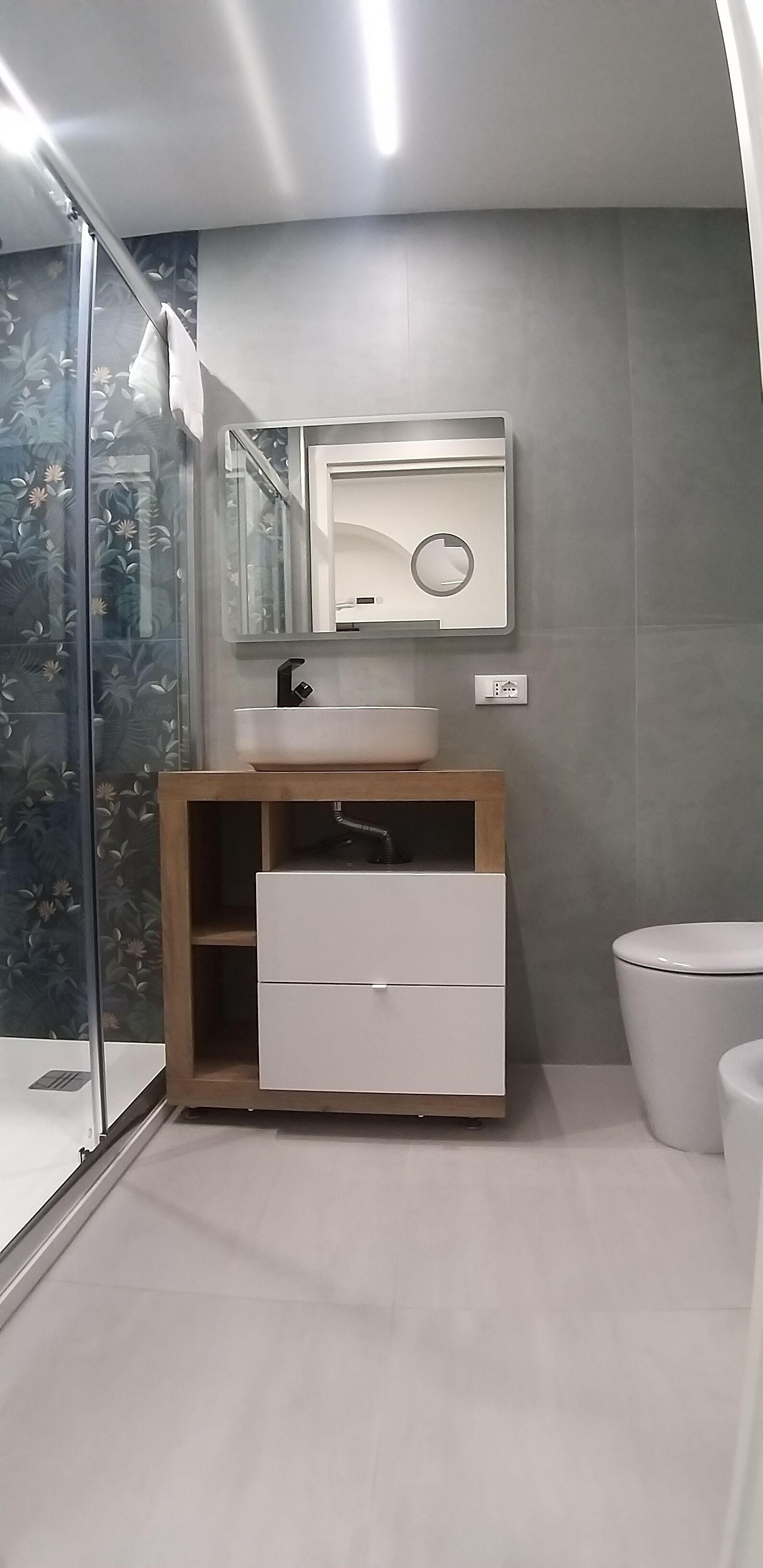 A modern bathroom with a glass shower enclosure, a wooden vanity with a sink and mirror, and a toilet.